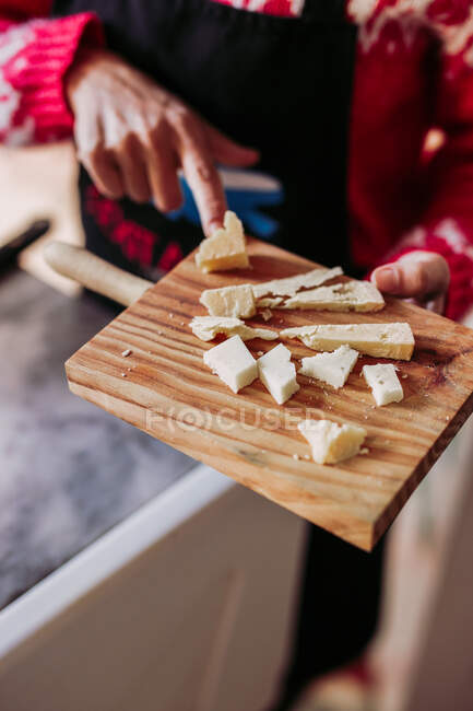 Побита анонімна доросла жінка в фартусі готує свіжий сир на дерев'яній дошці для різання, працюючи в затишній місцевій делікатній крамниці. — стокове фото