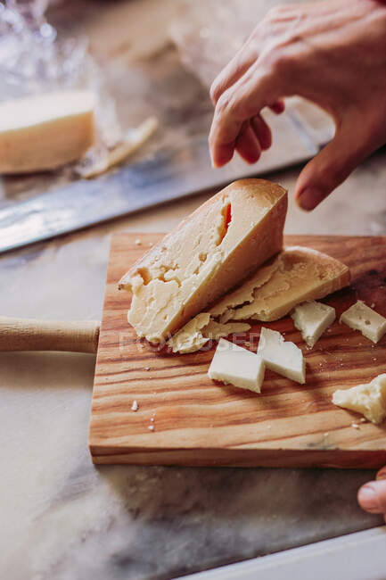 Zugeschnittene anonyme Person bereitet frischen Käse auf einem hölzernen Schneidebrett zu, während sie in einem gemütlichen lokalen Feinkostladen arbeitet — Stockfoto