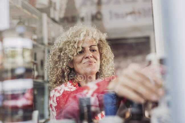 Happy adult woman with curly hair selling cheese in local food delicatessen store — Stock Photo