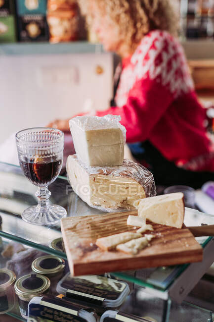 Mulher adulta anônima desfocada com cabelo encaracolado vendendo queijo e vinho na loja local de iguarias — Fotografia de Stock