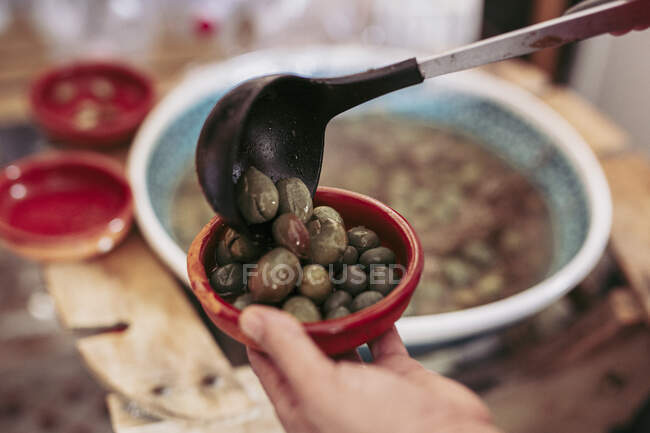 Unrecognizable person putting ladle of olives into bowl while working in local food store — Stock Photo