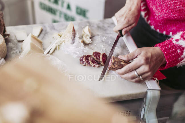 Von oben Unbekannter schneidet leckere Wurst auf Theke in Käsenähe, während er im örtlichen Lebensmittelgeschäft arbeitet — Stockfoto