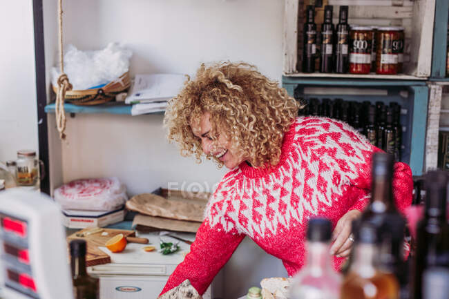 Дружелюбная взрослая женщина с вьющимися волосами работает в уютном местном магазине деликатесов — стоковое фото