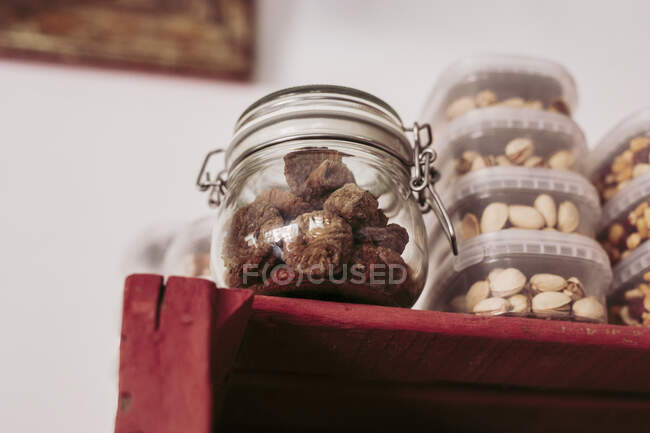 From below glass jar with truffles and plastic boxes with pistachios placed on red wooden shelf in local delicatessen food store — Stock Photo