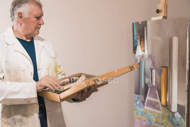 Старший художник, стоящий в домашней мастерской и выбирающий краски — стоковое фото