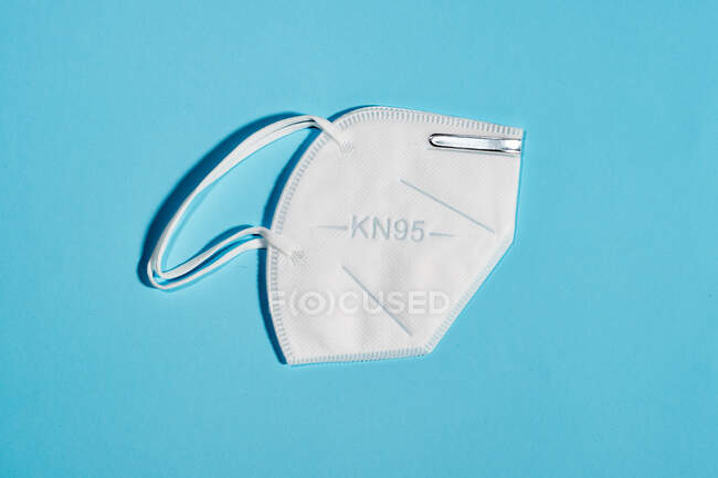 Máscara blanca con índice de protección KN95 reutilizable para la protección del virus sobre fondo azul claro - foto de stock