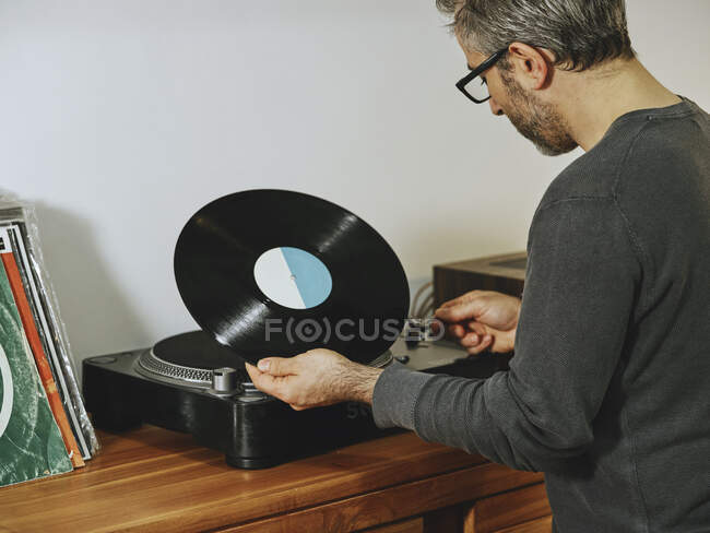 Vista lateral do homem sério definindo toca-discos e desfrutando de músicas em disco de vinil retro enquanto relaxa em casa — Fotografia de Stock