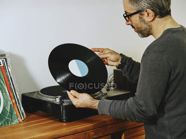 Вид сбоку на серьезного человека, сидящего за столом и наслаждающегося песнями на ретро-виниловом диске, пока охлаждаются дома — стоковое фото