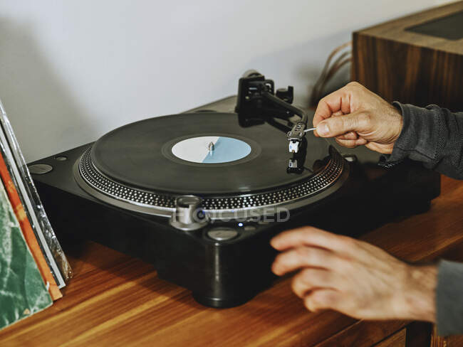 Cropped unrecognizable person setting turntable and enjoying songs on retro vinyl disc while chilling at home — Stock Photo