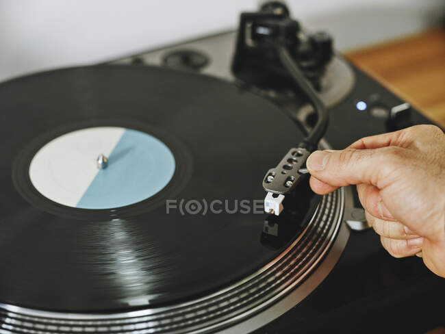 Von oben beschnittene Hände, die einen zeitgenössischen Plattenspieler mit Retro-Schallplatte auf einem Holztisch justieren — Stockfoto