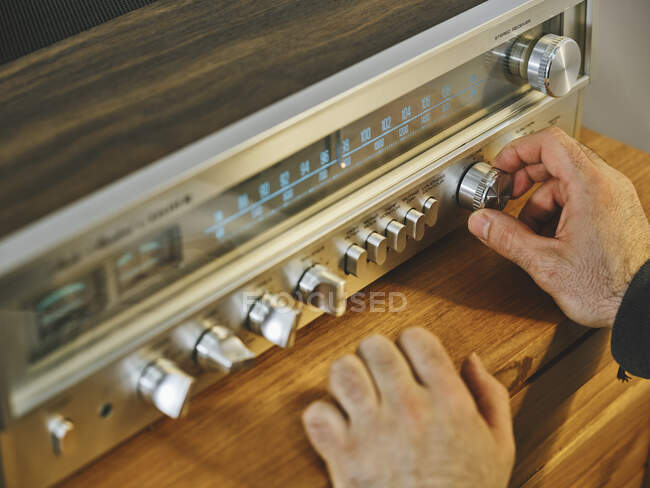 Alto ángulo de las manos de las cosechas de radio sintonización masculina irreconocible colocado en el estante de madera en la sala de estar - foto de stock