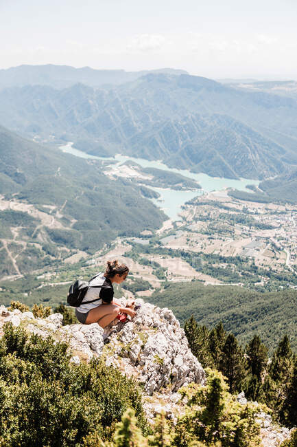 Back view of anonymous female tourist in casual clothes enjoying picturesque landscape while sitting on stony ground on sunny day in summer — Stock Photo