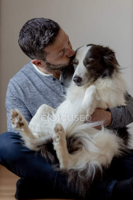 Homme en tenue décontractée donnant câlin et baiser au chien Border Collie bien-aimé tout en étant assis en position lotus sur le sol en bois — Photo de stock