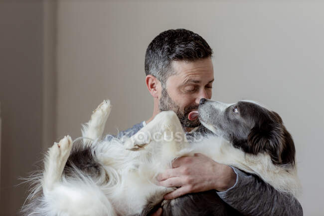 Homme en tenue décontractée donnant câlin et baiser à la frontière bien-aimée Collie chien à la maison — Photo de stock