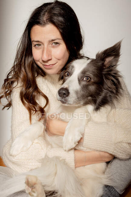 Caring female in woolen sweater hugging funny Border Collie dog while sitting on wooden floor together looking at camera — Stock Photo