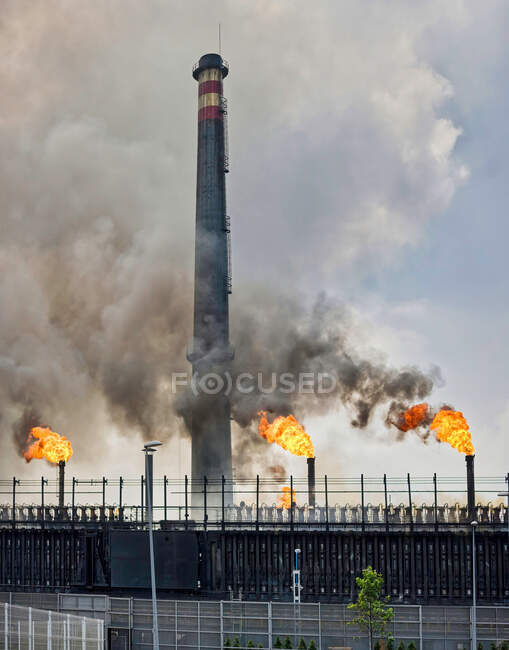 Weathered industrial buildings and pipes emitting smoke and flames at coking factory — Stock Photo
