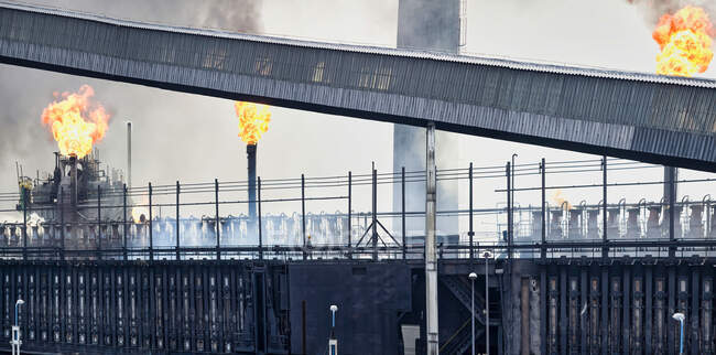 Weathered industrial buildings and pipes emitting smoke and flames at coking factory — Stock Photo