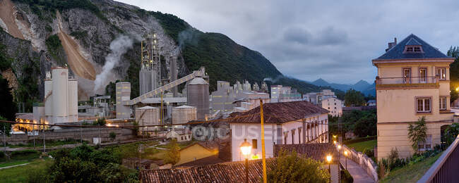 Panoramic scenery of vintage cottage on side of road and opening view of concrete factory behind mountain covered with trees in Spain — Stock Photo