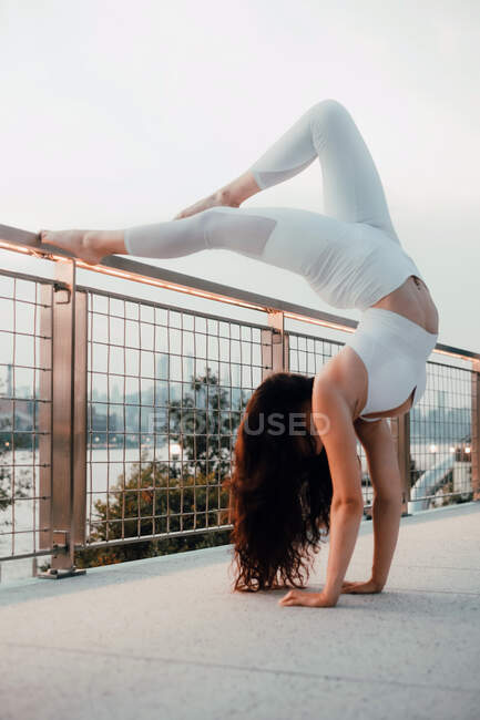Visão lateral de baixo ângulo da mulher flexível no sutiã esportivo e leggings realizando suporte escorpião durante o exercício descalço e inclinando-se sobre trilhos de metal na cidade — Fotografia de Stock