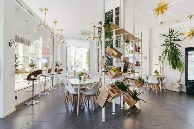 Innenarchitektur eines modernen hellen Restaurants mit Töpfen in Holzkiste als Dekoration und goldenen Lampen an weißen Decken über Tischen mit Stühlen — Stockfoto