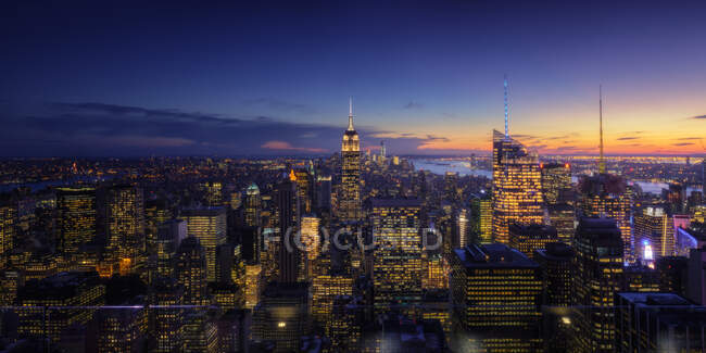 Beleuchtete Wolkenkratzer in der Innenstadt der modernen Stadt gegen bewölkten Himmel bei Sonnenuntergang — Stockfoto