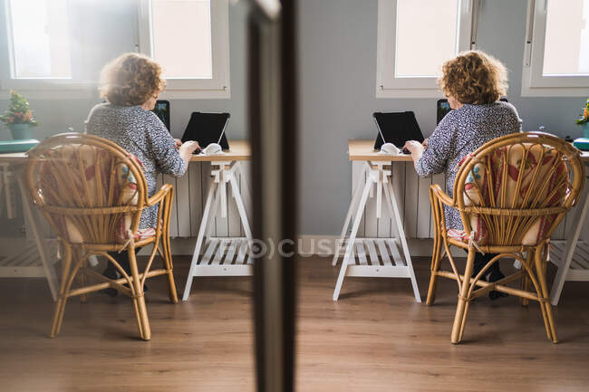 Vista laterale di donna adulta in vestiti occasionali che lavora su computer portatile in cuffie a camera decorata con cactus in pentole di ceramica — Foto stock