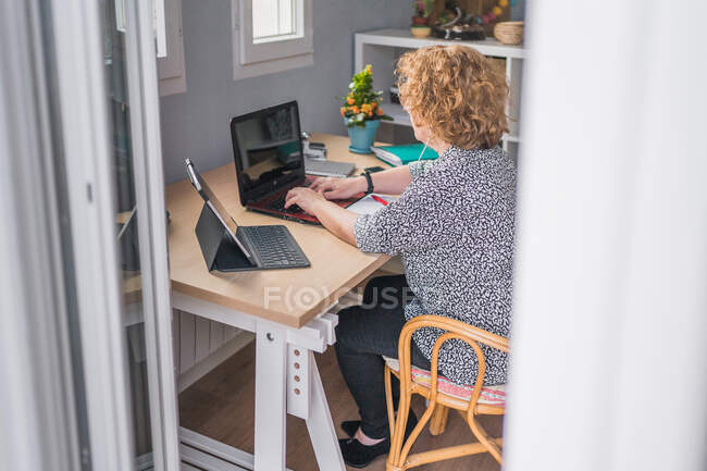 Vista laterale di donna adulta in vestiti occasionali che lavora su computer portatile in cuffie a camera decorata con cactus in pentole di ceramica — Foto stock