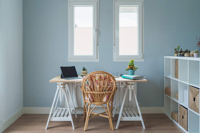Интерьер современной комнаты и рабочего места с деревянным столом с ноутбуком и папкой и креслом возле деревянных полок с коробками и горшками растений — стоковое фото