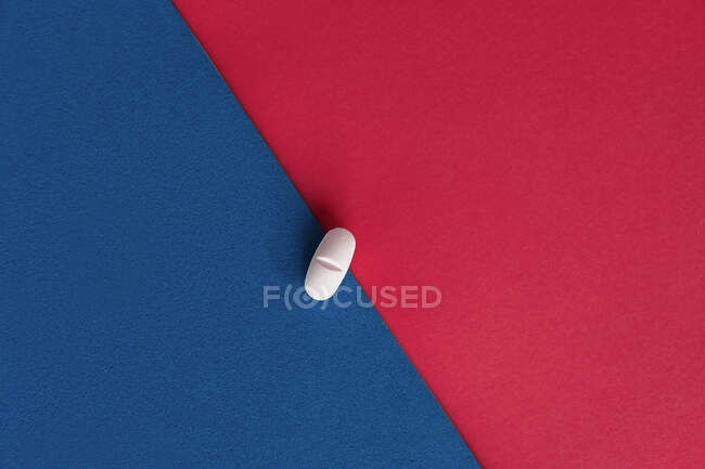 Vista superior de la píldora recetada para el tratamiento de la gripe colocada en hojas de papel rojas y azules - foto de stock