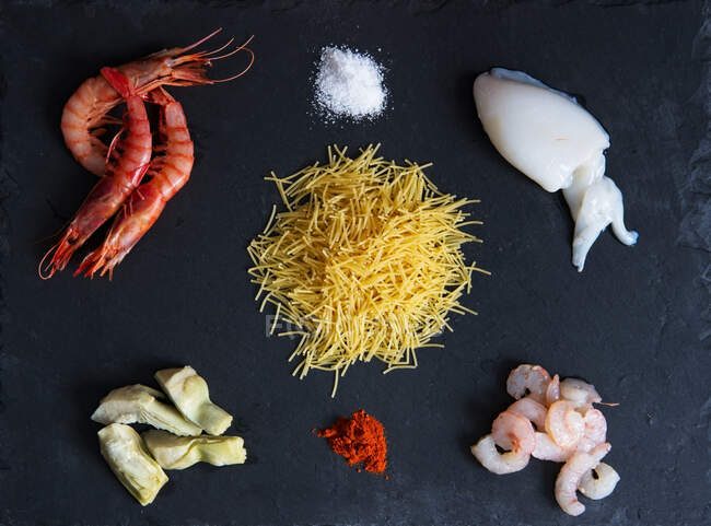 Vista superior de los camarones crudos y el filete de calamar colocado en la superficie oscura con pilas de sal y pimentón - foto de stock