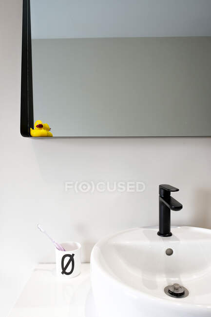 Сучасний інтер'єр домашньої ванної кімнати з білим керамічним умивальником і гумовою качкою, розміщеною на чорному дзеркалі — стокове фото