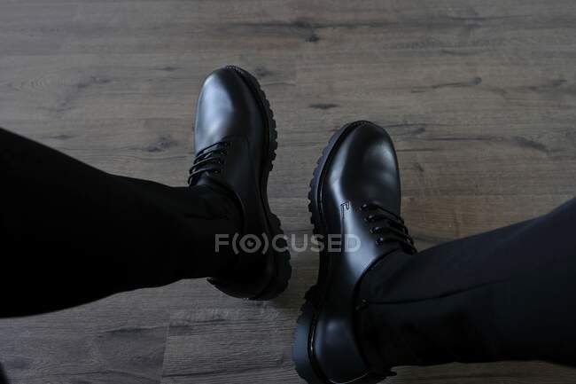 Male feet in casual clean pair of black boots on wooden floor — Stock Photo