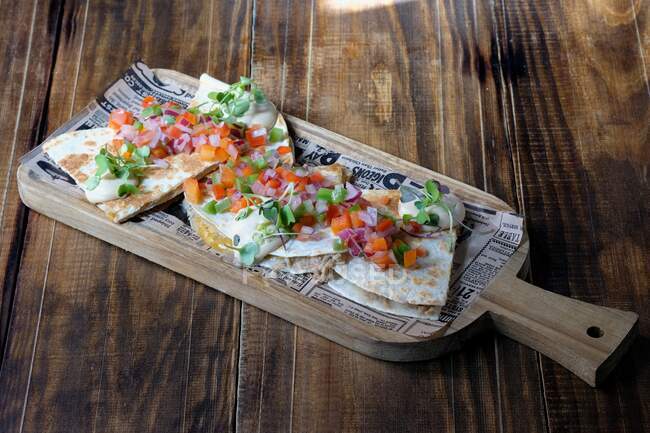 Alto ángulo de plato mexicano hecho de tortilla llena de queso y adornada con verduras frescas en la parte superior mientras se coloca en la mesa de madera en el restaurante - foto de stock