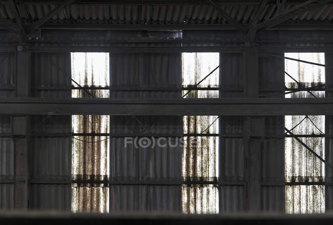 Стара іржава металева стіна з яскравими променями пробивного світла з протилежних вікон, що знаходяться всередині покинутого покинутого будинку фабрики в Іспанії. — стокове фото