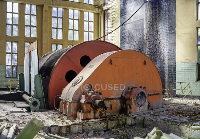 Industrial circular machine with metal mechanism locating inside deserted ownerless dilapidated industrial workshop with light walls and large arched windows — Stock Photo