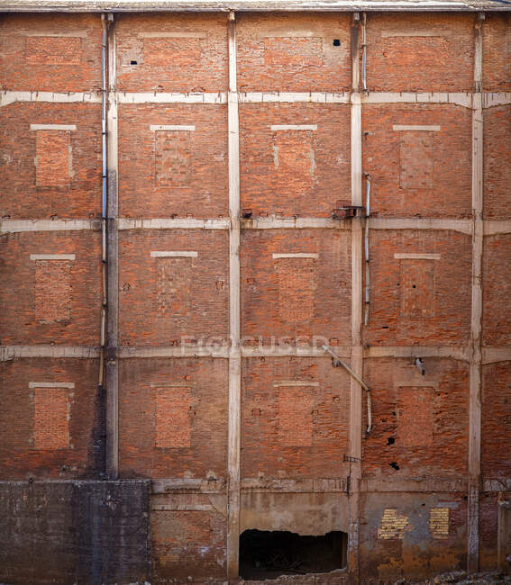 Обветшалая старая высокая стена заброшенного здания из красного кирпича с кирпичными окнами разрушенный вход и трубы с грязными черными пятнами — стоковое фото
