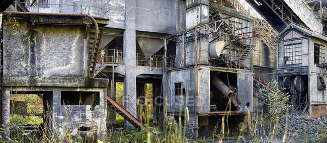 Gray concrete dilapidated industrial buildings of abandoned coal mine with various metal ladders and pipes locating on blockages of coal — Stock Photo
