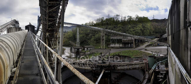 Старые заброшенные нежилые промышленные здания с тележками для перевозки угля в сельской местности с видом на зеленые горы на заброшенной угольной шахте в пасмурный день — стоковое фото