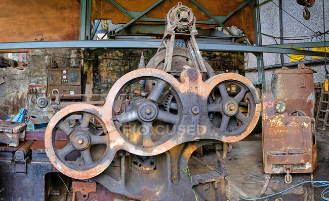 Alter gebrauchter rostiger Mechanismus aus Stahlscheiben verschiedener Durchmesser, montiert auf Metallvorrichtung in schmutzigem, verlassenem Fabrikgebäude — Stockfoto
