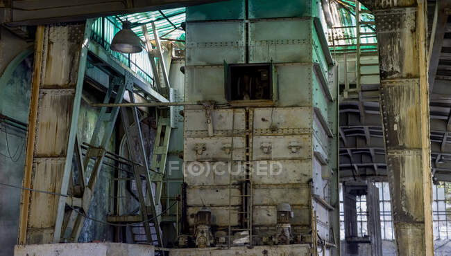 Rusty old tall multi level metal tower with iron staircase leading to small open window in middle of structure surrounded by metal beams in abandoned building of coal mine — Stock Photo