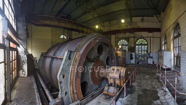 Destruida máquina circular industrial oxidada con mecanismo metálico y tanques ubicados en un taller industrial en ruinas descuidado con ventanas arqueadas - foto de stock