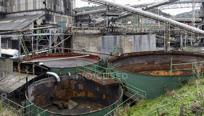 Desde arriba de enormes tanques de agua vacía de metal oxidado pintados de verde rodeado de varias estructuras en ruinas y carros para el transporte de carbón en la mina de carbón abandonada ociosa - foto de stock