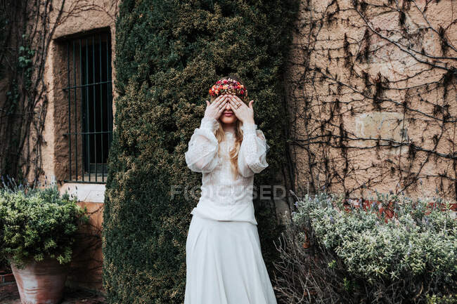 Happy bride covering eyes near bush — Stock Photo