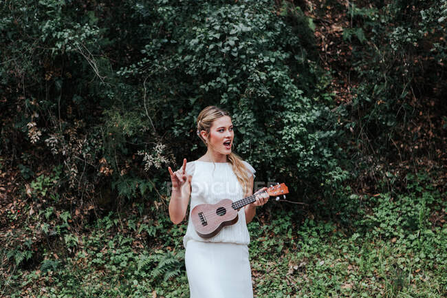 Веселая невеста играет на укулеле возле кустов — стоковое фото