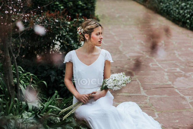 Junge Braut sitzt auf Weg im Garten — Stockfoto