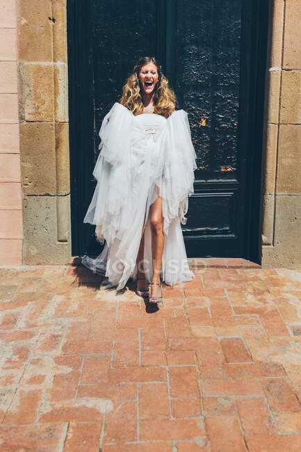 Glückliche junge Braut im weißen Hochzeitskleid tanzt am Eingang des Altbaus — Stockfoto
