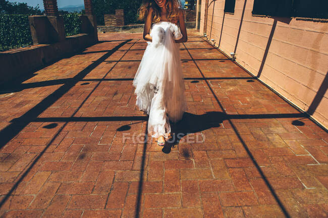 Happy young bride in white wedding dress walking near entrance of old building — Stock Photo