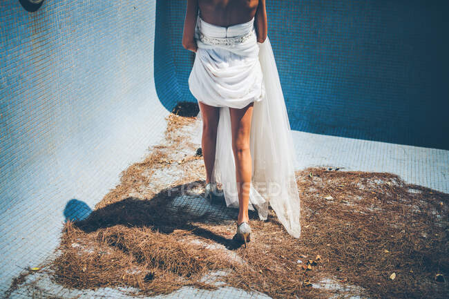 Sinnliche junge Braut in stylischem weißen Brautkleid steht im leeren Pool — Stockfoto