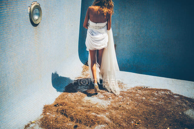 Чуттєва молода наречена в стильній білій весільній сукні, що стоїть у порожньому басейні — стокове фото