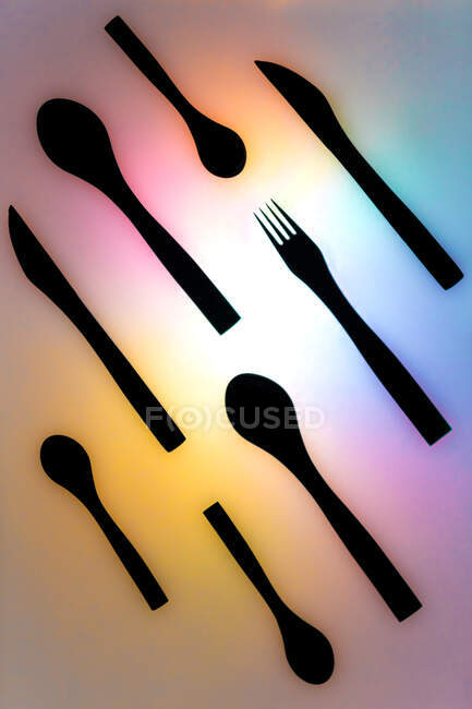 Вид зверху композиція чорних столових приборів, розташованих на освітленій неоновій різнокольоровій поверхні — стокове фото